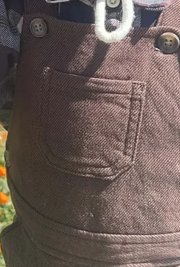 Détail d'une salopette en toile brune : poche plaquée et boutons métalliques.